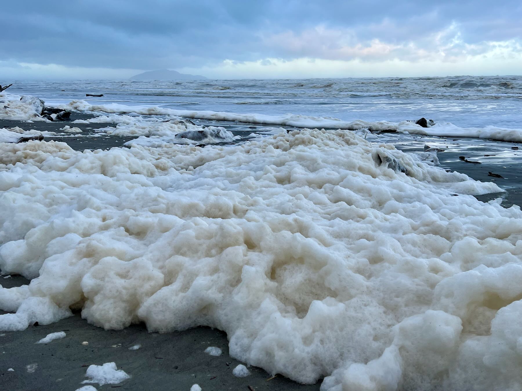 A frenzy of sea foam, with Kāpiti Island in the background. 