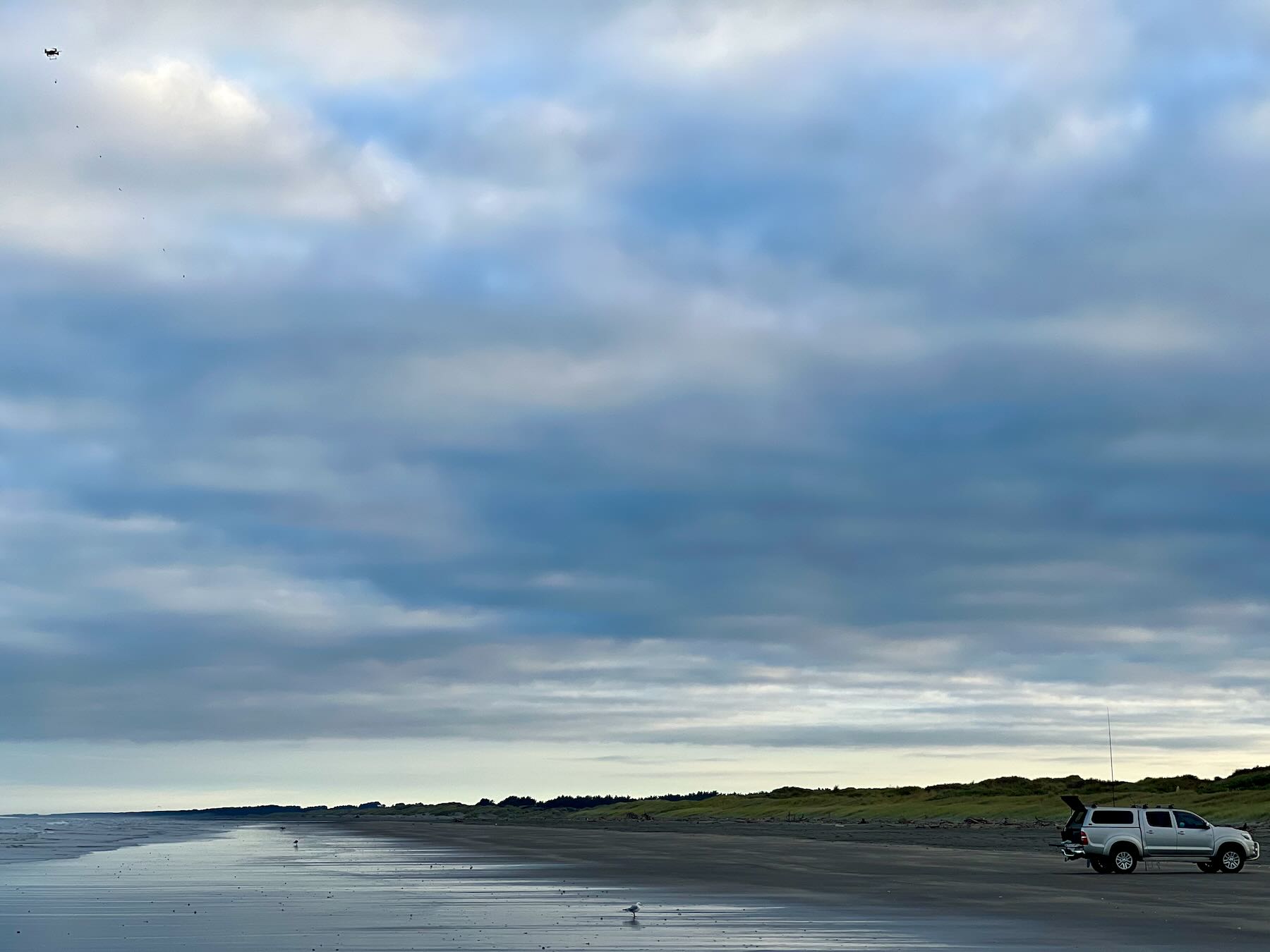Vehicle on the beach with upright rods beside it and a drone at top left of the photo. 